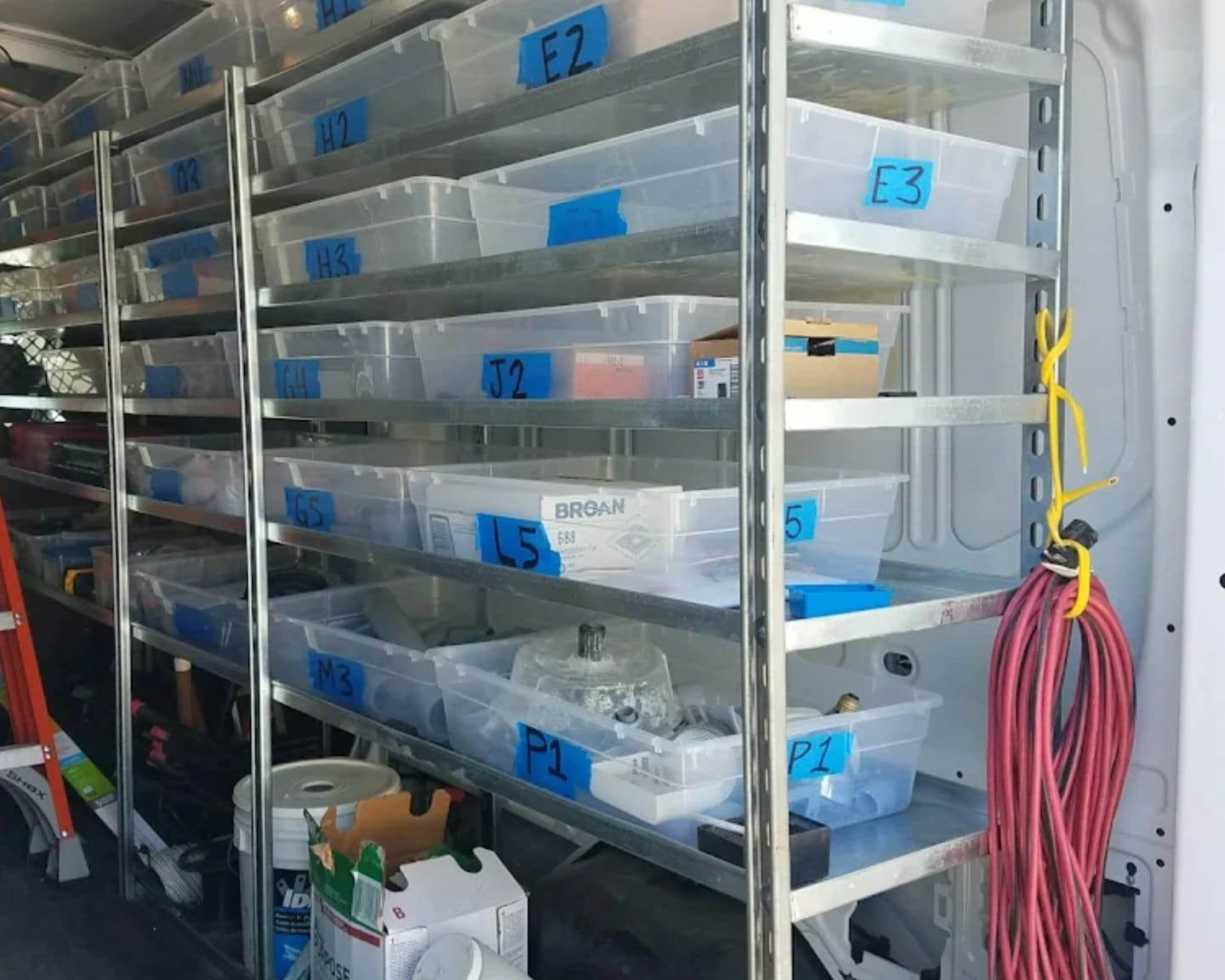 Servis minibüsünün içindeki etiketli kutularla düzenlenmiş metal raflar.